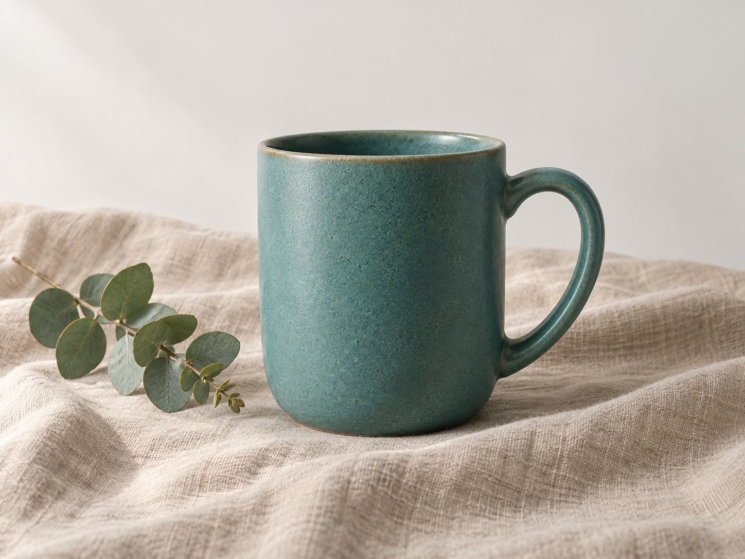 Converted sample: a teal ceramic mug on linen beside eucalyptus leaves